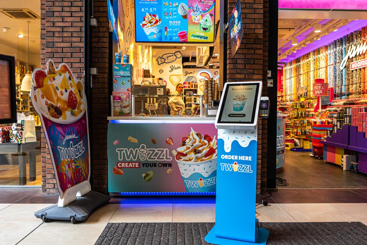 Onesix Kiosk in custom branding at the entrance of an ice cream and sweets shop, with a staff member behind the counter