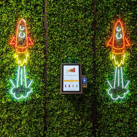 Onesix Kiosk Pro Wall on a green plant wall between neon rockets